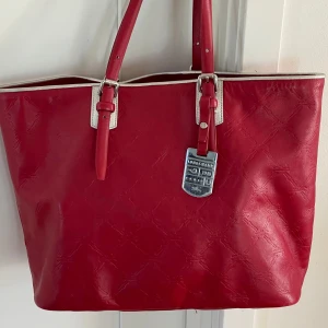 Longchamp Leather Tote - Sällsynt Longchamp tote bag. Präglad l monogramlogotyp på läder. Röd med metallic-silverkant. Hängande medtalplatta. Magnetisk stängning. Invändig ficka med dragkedja. Avtagbar kosmetikapåse m dragkedja. En mindre fläck i botten av väskan, bild 5.