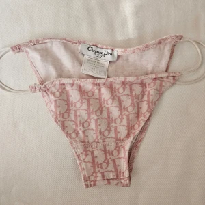 Christian Dior underdel / trosa / lingerie  - Ikonisk underdel från Christian Dior med den klassiska loggan i rosa. Snörena på sidan är i resår. 95% cotton 5% lycra. Storlek 38 men skulle säga att dom passar 34/36. Från år 2000 ca men helt oanvända.  rosa bikinunderdel loungelkäder lounge logo