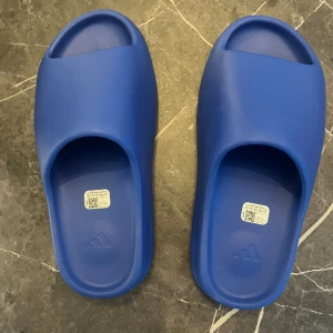 Blå Adidas slides - Säljer ett par Yeezy slides som jag har köpt från Adidas CONFIRMED, dom är i colorwayen blå/azure och kvitto finns.🧾✅ Dom är helt nya/aldriganvända och dom är i storlek 44.5