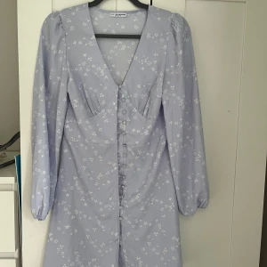 Mini klänning - En kort ljusblå/ljuslila klännning med knappförslutning nästan hela vägen. Från kollektionen Nelly X Glamorous! Storlek 36. Köparen står för frakt 🌸