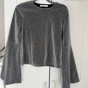 Glittrig topp med trumpetärm  - En glittrig topp med ballongärm från NA-KD! Perfekt till festligare tillfällen!  Lappen kvar från köpestillfället.  Storlek 36. Köparen står för frakt! 🌸