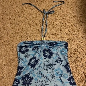 Blå blommig topp - Säljer en superfin blå topp med blommigt mönster och textdetaljer. Den har knytband runt nacken med färgglada pärlor som ger en söt touch. Perfekt för sommarens stranddagar! 💙
