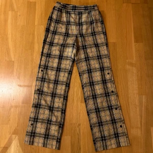 Rutiga byxor med knappar - Säljer ett par snygga rutiga byxor i beige och svart från Stradivarius. De har en hög midja och raka ben med  knappar längs sidorna. Sjukt sköna 