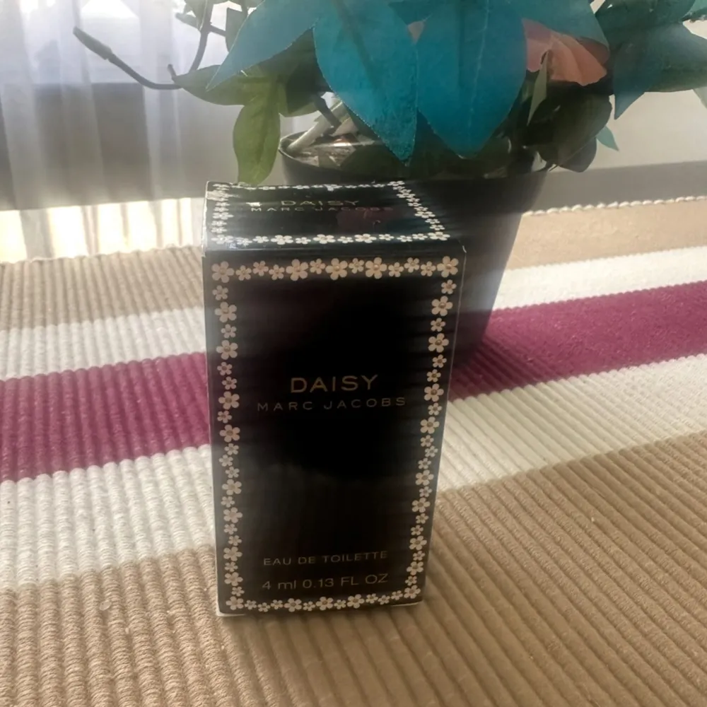 Säljer en söt liten flaska Daisy Eau de Toilette från Marc Jacobs. Förpackningen är svart med små vita blommor runt kanterna, vilket ger en fräsch och blommig känsla. Perfekt för att ha med sig i väskan! Flaskan rymmer 4 ml.. Parfym.