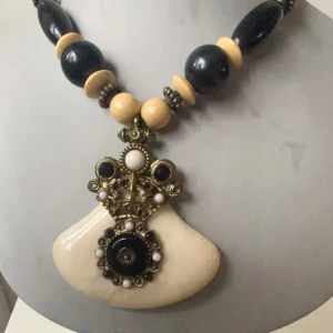 Unikt halsband med stora pärlor och hänge - Säljer ett unikt halsband med stora svarta och beige pärlor. Det har ett stort dekorativt hänge med detaljer i brunt och beige. Perfekt för att ge en bohemisk touch till din outfit. Passar både till vardag och fest!