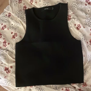 Svart ärmlös topp från Vero Moda  - Säljer en stilren svart ärmlös topp från Vero Moda. Perfekt för både vardag och fest. Toppen har en enkel och elegant design som gör den lätt att matcha med olika outfits. Passar bra till både jeans och kjol. 🖤 osäker på storleken men passar nog från xs-m då den e stretchig, blir kortare så större storlek så de bror på hur kort man vill ha den.