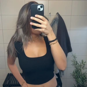 Svart croppad topp - Säljer en snygg svart croppad topp med fyrkantig urringning. Perfekt för både vardag och fest! Toppen är tight och framhäver figuren på ett stilrent sätt. Passar bra till jeans eller kjol för en trendig look.