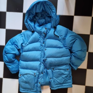 Blå dunjacka från Bik Bok - Säljer en supermysig blå dunjacka från Bik Bok. Perfekt för kalla vinterdagar med sin tjocka vaddering av 70% dun och 30% fjäder. Jackan har en stor huva och praktiska fickor med knappar. Den är i mycket bra skick och redo för nya äventyr! 💙