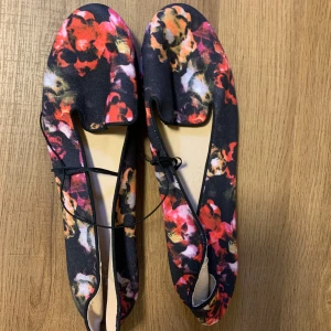 Blommiga ballerinaskor/loafers i storlek 40 från HM - Säljer ett par snygga ballerinaskor med ett färgglatt blommönster i rött, rosa och svart. Skorna är helt nya och är perfekta för vår och sommar. De har en bekväm passform och är lätta att matcha med olika outfits. Perfekta för både vardag och fest!