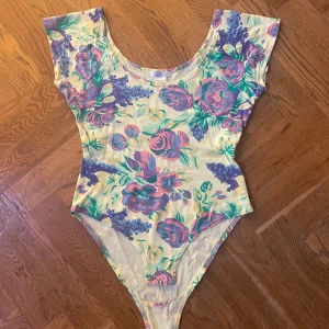 Blommig body från Sweet Laundry - Säljer en superfin blommig body från Sweet Laundry i storlek M. Den har en härlig mix av rosa och lila blommor på en ljusgul bakgrund. Materialet är mjukt och stretchigt med 95% bomull och 5% elastan. Perfekt för sommardagar eller en festlig kväll! 🌸