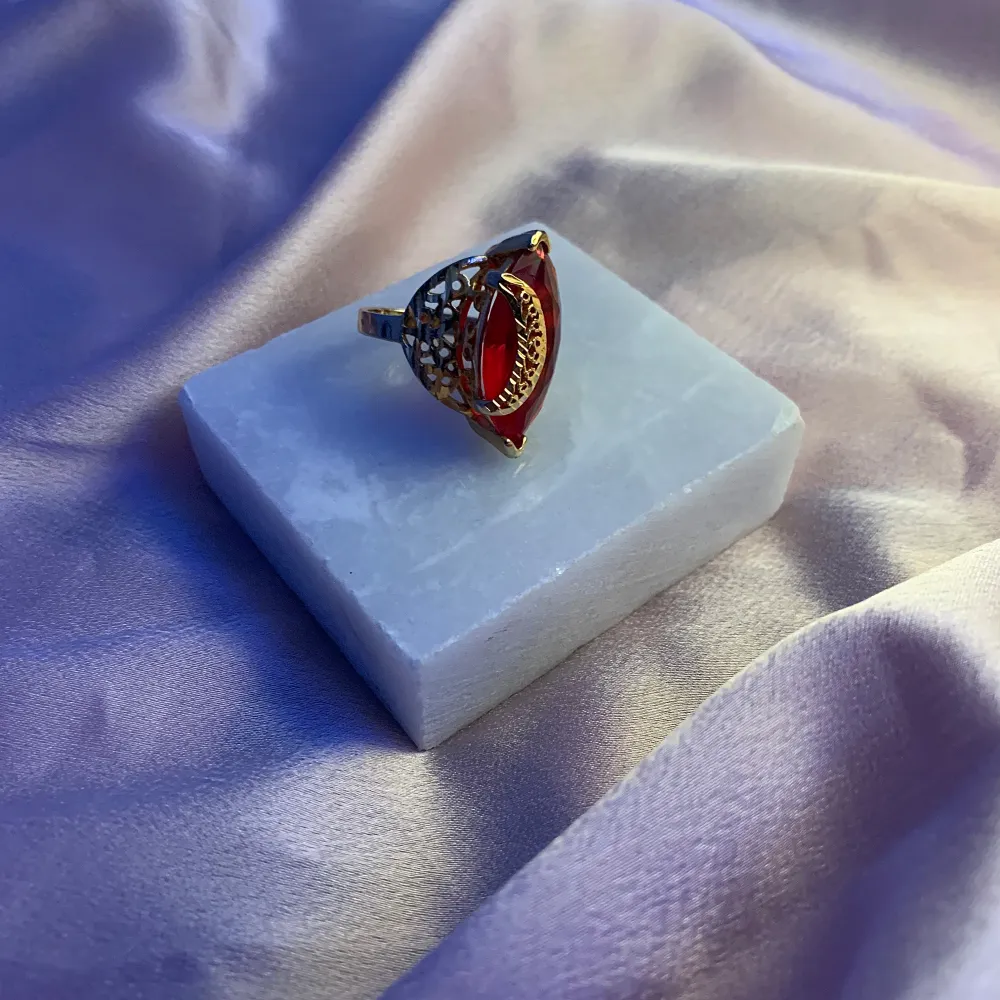 Snygg guldfärgad ring med en röd detalj i mitten. Ringen har en unik design med ett bladliknande mönster som ger den en elegant touch. Perfekt för att piffa upp vilken outfit som helst, oavsett om det är till vardags eller fest.. Accessoarer.