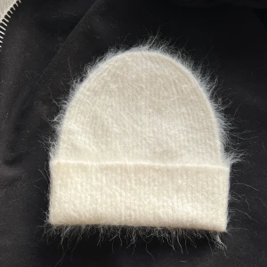 Vit fluffig mössa - Mysig vit mössa i fluffigt material, perfekt för kyliga dagar. Den har en enkel design med uppvikt kant som ger extra värme och stil.