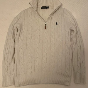 Vit stickad tröja från Polo Ralph Lauren - Säljer en stilren vit stickad tröja från Polo Ralph Lauren med kabelstickat mönster och dragkedja vid halsen. Tröjan har långa ärmar och en broderad logotyp på bröstet. Perfekt för kyliga dagar! Lämna gårna prisförslag 😁