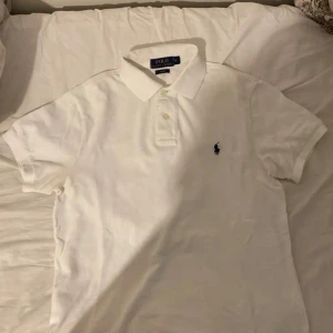 Vit pikétröja från Ralph Lauren - Säljer en klassisk vit pikétröja från Ralph Lauren i slim fit. Tröjan har korta ärmar och en broderad logotyp på bröstet. Perfekt för en stilren look.