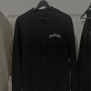 Svart jacka från Jack Daniel's - Snygg svart jacka med Jack Daniel's-logga på bröstet och ryggen. Jackan har knappar framtill och långa ärmar. Perfekt för en casual look. Vann den på en tävling men inte använt den. Storlek M. Kan gå med på nån deal, skicka iväg ett pris/fråga!