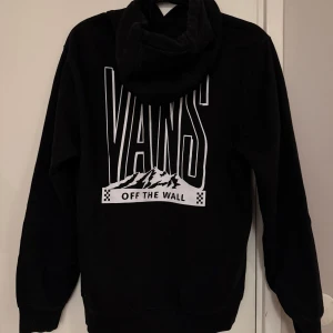 Svart hoodie från Vans - Säljer en svart hoodie från Vans med tryck på baksidan. Tröjan har en klassisk design med huva och långa ärmar. 