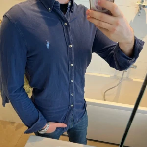 Blå skjorta från Ralph Lauren - Snygg blå skjorta från Ralph Lauren med klassisk krage och knappar framtill. Skjortan har en broderad logotyp på bröstet och långa ärmar. Perfekt för en stilren look. 