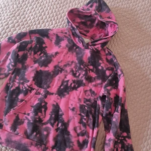 Rosa och svart hoodie med batikmönster - Cool hoodie i rosa och svart med batikmönster. Den har en stor ficka framtill och en bekväm huva. Perfekt för en avslappnad stil.