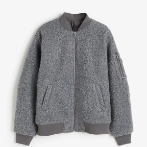 Grå bomberjacka i ull - Snygg grå bomberjacka i ull med dragkedja framtill. Jackan har ribbade muddar vid ärmslut och nederkant samt en praktisk ficka på ärmen. Perfekt för kyligare dagar. 