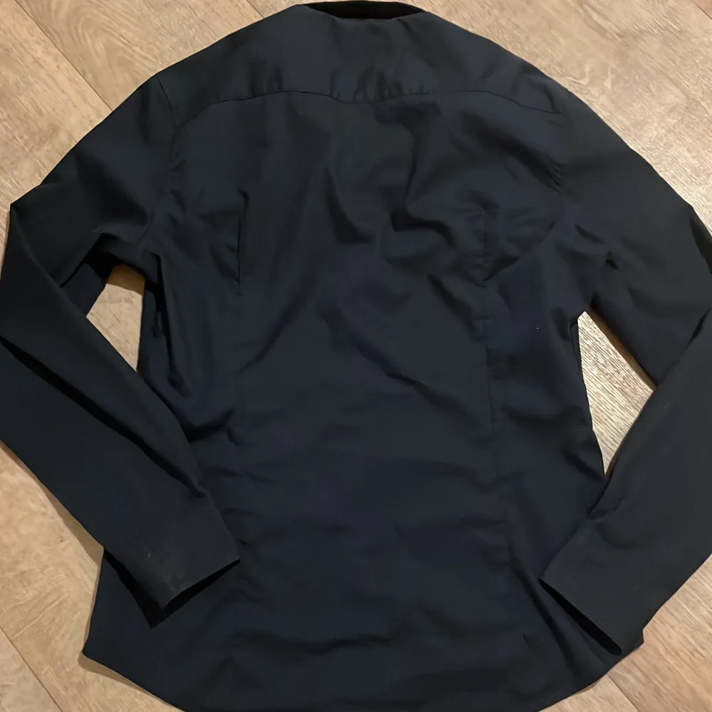 Snygg mörk blå fit skjorta från H&M med knappar framtill. Perfekt för en stilren look. Skjortan är tillverkad i ett lättskött material som är enkelt att stryka. Priset kan diskuteras!. Paidat.