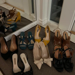 Samling av klackskor i olika färger - En stilfull samling av klackskor i olika färger och stilar. Inkluderar svarta, beige och gula pumps, samt blå och bruna sandaler med klack. Perfekt för att komplettera din garderob med eleganta alternativ.