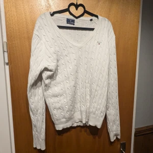 Vit stickad tröja från Gant - Säljer en stilren vit stickad tröja från Gant med klassiskt kabelstickat mönster. Tröjan har en v-ringad hals och långa ärmar, perfekt för kyligare dagar. En tidlös design som passar till många tillfällen. I gott skick.