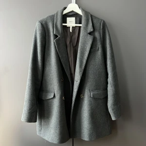 Grå kappa   - Elegant grå kappa. Den har en klassisk design med knappar framtill. Perfekt för kyligare dagar till vår/höst. 