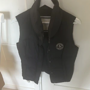 Mörkblå dunväst från Abercrombie and Fitch - Snygg svart dunväst från Abercrombie & Fitch med dragkedja och hög krage. Västen har en diskret logga på bröstet.