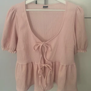 TIE FRONT TOP - Söt rosa blus med korta puffärmar och knytning framtill. Blusen har en v-ringad design och är tillverkad i ett lätt och luftigt material.