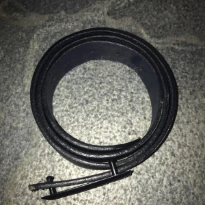 Dsq Svart bälte med kanadensisk lönnlövdetalj - Snyggt svart bälte från DSQ med en unik spänne som har en röd kanadensisk lönnlövdetalj. Perfekt för att ge en stilren touch till din outfit. Bältet är tillverkat i ett robust material och har en modern design. 