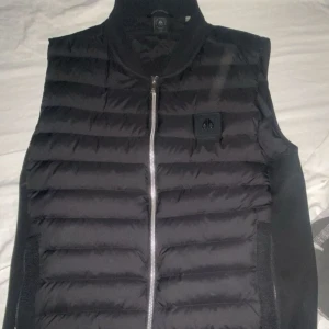 Svart moose knuckle dunväst med dragkedja -  svart dunväst med dragkedja och en stilren design. Använd i ca 5 månader inga skador eller något så kvaliten är 10/10 . Storlek S men funkar även till viss M