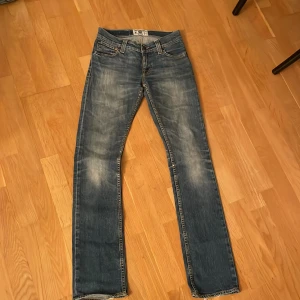 Blå jeans från Tiger of Sweden - Snygga blå jeans från Tiger of Sweden med klassisk femficksdesign och orange sömmar. De har en rak/bootcut passform och är perfekta för en avslappnad stil. Märkeslogga på insidan av linningen.💗