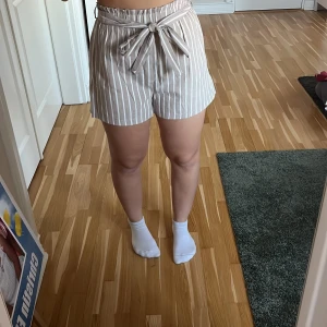 Randiga linneshorts  - Säljer ett par beige och vita randiga linneshorts från Shein. De har en bekväm midwaist passform med knytband i midjan 🌟