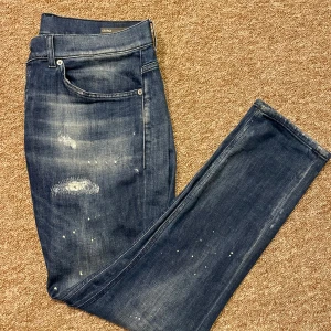 Blå jeans med slitningar - Snygga blå jeans från dondupmed coola slitningar och en lätt tvättad look. De har en klassisk femficksdesign och knappgylf. Perfekta för en stilig look, producerad i italien och modellen är george🇮🇹🍾