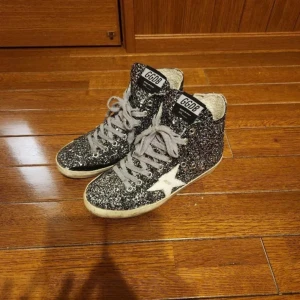 Svarta glittriga sneakers från golden goose - Snygga svarta sneakers från golden goose med glittrig yta och vit stjärndetalj på sidan. Skorna har snörning och dragkedja för enkel på- och avtagning. Perfekta för att ge din outfit en extra touch av glamour.