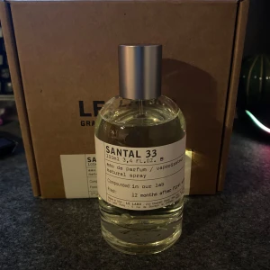 Santal 33 Eau de Parfum från Le Labo - Säljer en flaska Santal 33 Eau de Parfum från Le Labo. Flaskan rymmer 100 ml och kommer i originalförpackning. Doften är känd för sina träiga och kryddiga noter, perfekt för den som gillar unika och långvariga parfymer. Flaskan har en minimalistisk design med en enkel etikett och en metallkork.