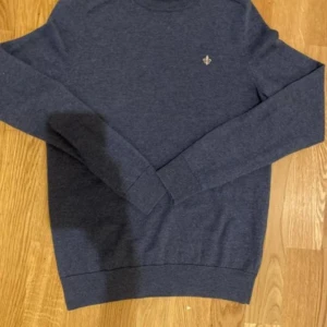 Morris tröja - Snygg mörkblå tröja med en liten broderad detalj på bröstet. Tröjan har långa ärmar och en klassisk passform, perfekt för kyligare dagar. Den är i storleken S men sitter som ett xs.🔥