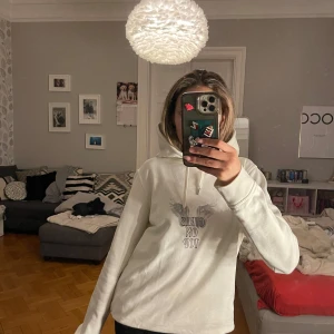 Vit hoodie med tryck från ganni  - Säljer en vit hoodie med texten 'Girls on Top' och ett vingmotiv på framsidan. Tröjan har en klassisk huva med dragsko och långa ärmar. Perfekt för en avslappnad stil.