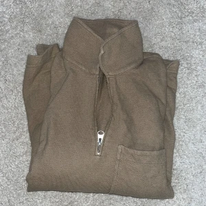 Beige tröja med dragkedja - Grabbkofta. Säljer en stilren beige tröja med dragkedja och hög krage. Tröjan har en praktisk bröstficka och är tillverkad i ett mjukt material. Perfekt för kyligare dagar.