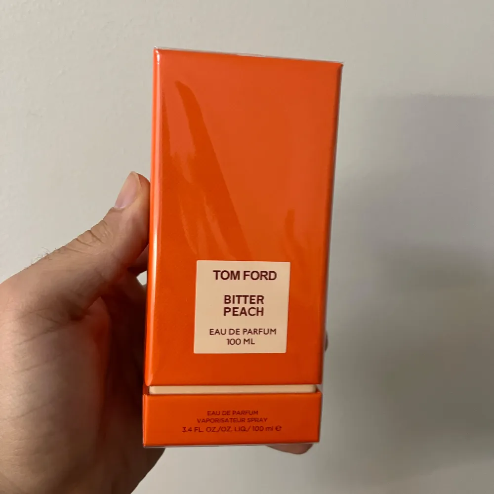 Tom Ford Bitter Peach Eau de Parfum i en elegant orange förpackning. Flaskan innehåller 100 ml av denna lyxiga doft som kombinerar fruktiga och bittra toner för en unik upplevelse. Perfekt för den som vill ha en djärv och sofistikerad doft.. Perfume.