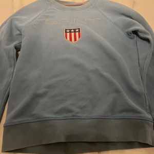 Blå sweatshirt från GANT - Säljer en ljusblå sweatshirt från GANT. Tröjan har långa ärmar och rund halsringning. Perfekt för en avslappnad stil. Enda defekten på den är att armbågarna är slitna, se bild 3 