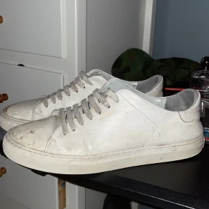 Vita sneakers från Axel Arigato - Säljer ett par vita sneakers från Axel Arigato med snörning. Skorna har en stilren design med en diskret logga på sidan. Perfekta för en avslappnad stil.