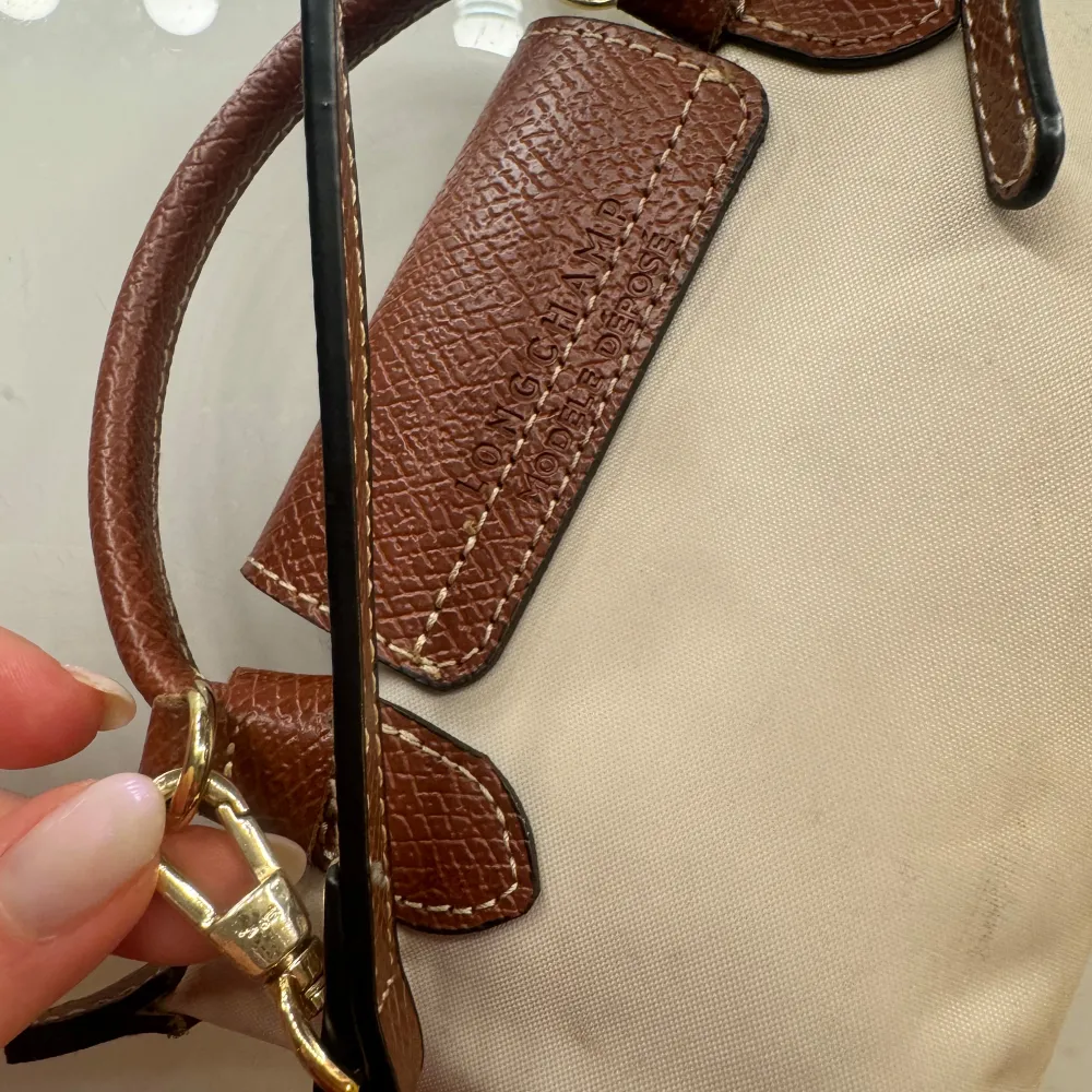 Säljer en stilren beige axelväska från Longchamp med bruna skinnremmar och detaljer. Väskan har en praktisk knappstängning och en elegant design som passar perfekt för vardagsbruk. Den är lätt att bära och har en tidlös look. Har ej kvar kvitto . Laukut & Käsilaukut.