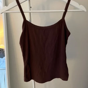 Brun ribbad linnetopp - Säljer en stilren brun ribbad linnetopp med smala axelband. Perfekt för varma dagar eller som ett lager under en tröja. Enkel och mångsidig design.