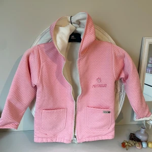 Rosa jacka med luva från Petrollio - Säljer en söt rosa jacka med luva  från Petrollio. Jackan har en dragkedja framtill och två praktiska fickor. Den är fodrat  med  jätte mjuk varm insida  . Perfekt för kyliga dagar!. Passar för 5,6 åring 