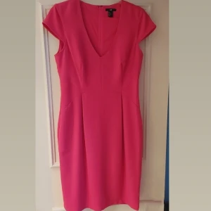Rosa klänning från H&M - Snygg rosa klänning från H&M med v-ringning och korta ärmar. Klänningen har en dragkedja i ryggen och är perfekt för en färgglad look. Den är tillverkad i ett mjukt material som ger en bekväm passform.