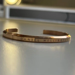 Rosé guldarmband från Daniel Wellington - Elegant guldarmband från Daniel Wellington. Armbandet har en slät yta med märkets namn ingraverat. Armbandet är aldrig använt och är köpt för 699kr. Färgen: Rose gold OBS. Du får lådan med armbandet!