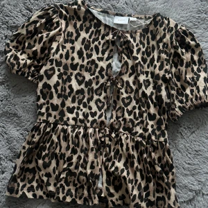 Leopardmönstrad blus med knyt - Trendig leopardmönstrad blus med korta ärmar och knyt framtill. Perfekt för att ge en djärv touch till din outfit. Toppen passar super för mig som brukar ha S och XS i toppar 