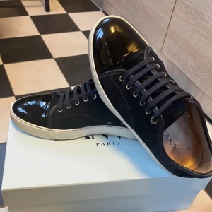 Marinblå  sneakers från Lanvin - Snygga marinblå sneakers från Lanvin med glansig tå och snörning. Skorna har en vit sula som kontrasterar mot det svarta materialet. Perfekta för en stilren look.