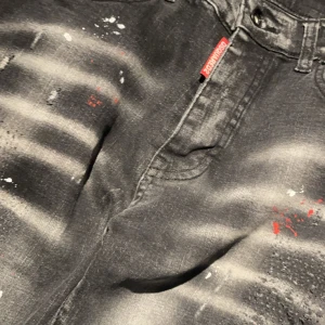 Svarta jeans från Dsquared2 - Snygga svarta jeans från Dsquared2 med coola slitningar och färgstänk i rött och vitt. De har en modern, distressed look och en klassisk femficksdesign. Perfekta för en edgy stil! Helt nya ej använda.